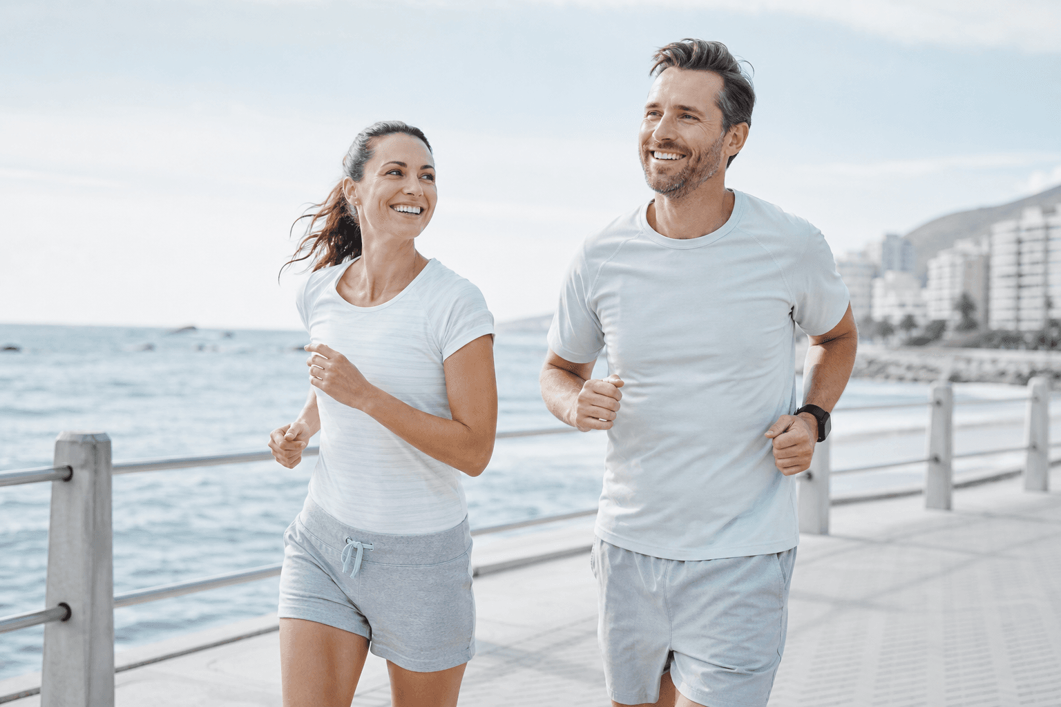 Two healthy adults jog together along a bright waterfront path in soft morning light